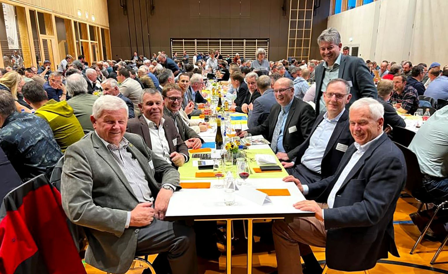 Mario Fehr und Ernst Stocker sitzen mit zahlreichen weiteren Personen an einem Tisch in der sehr gut gefüllten Irchelhalle. 