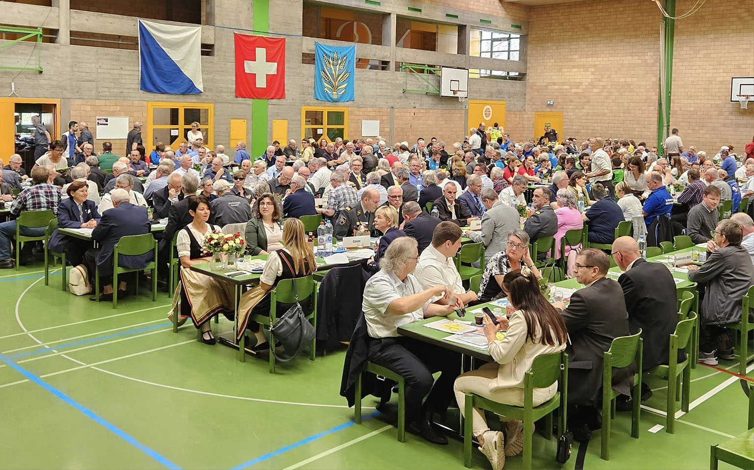 Zahlreiche Personen sitzen an der DV an Festbänken in der Halle, im Hintergrund hängen Fahnen.