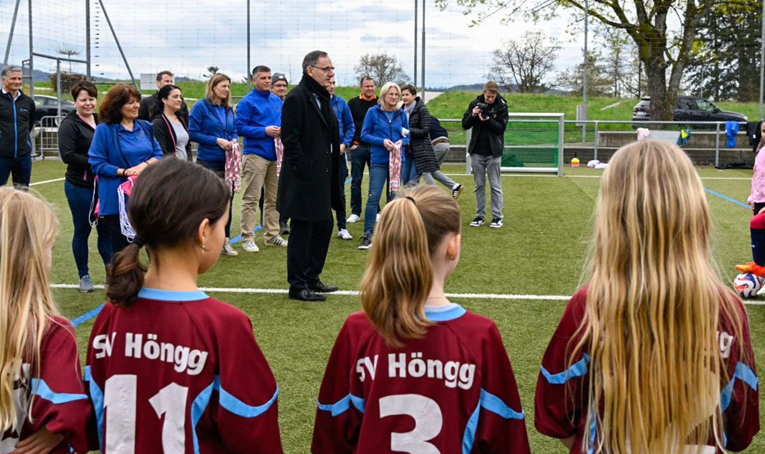 Mario Fehr steht mit den anderen Medienkonferenz-Teilnehmenden auf dem Fussballplatz in Höngg und be...