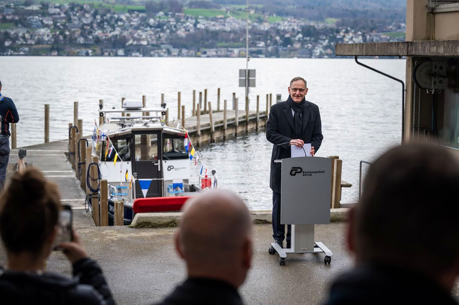 Mario Fehr steht am Rednerpult am Ufer, im Hintergrund das neue Schiff. 