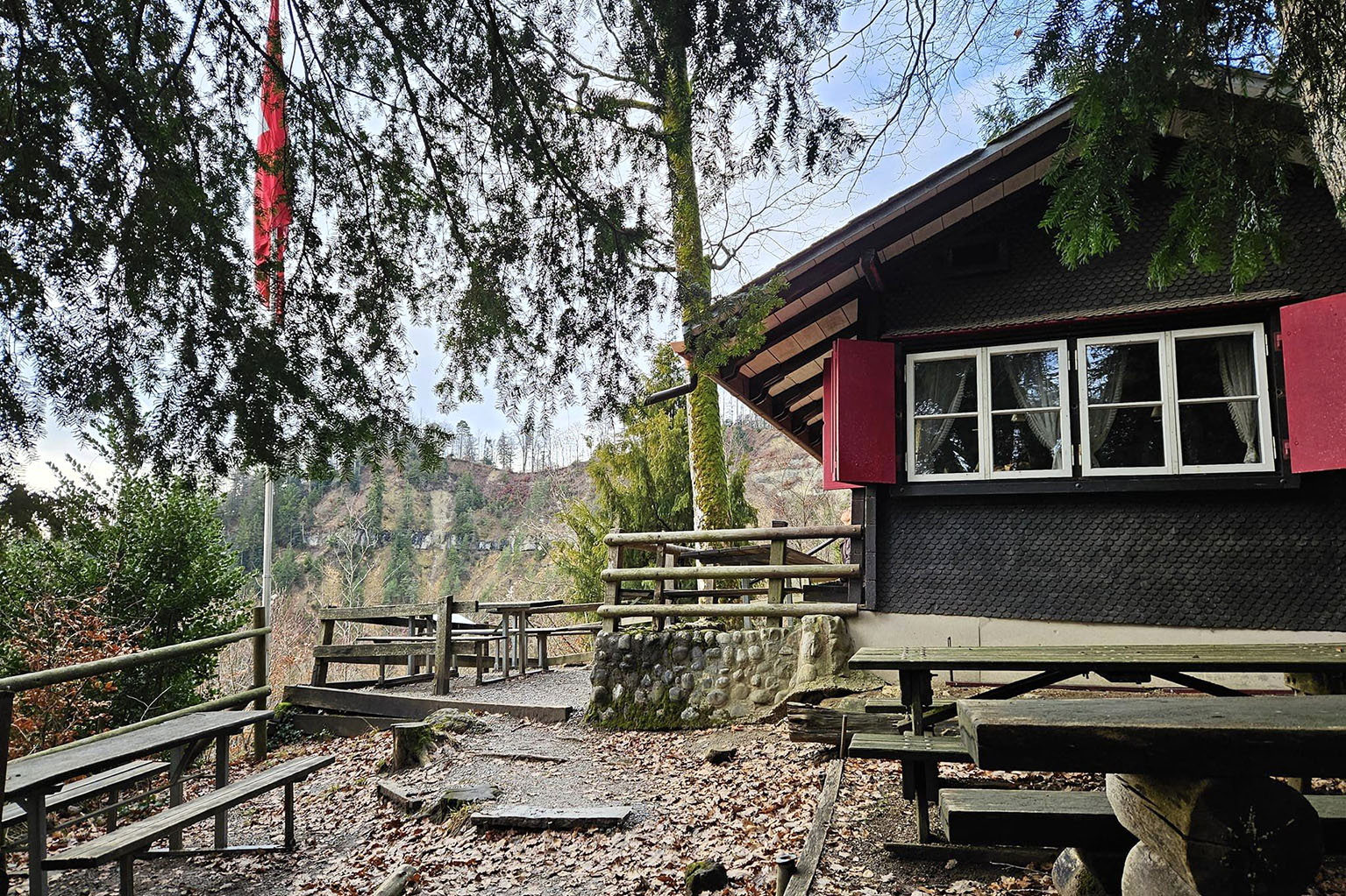 Blick auf das Teehüsli von aussen, mit Sitzbänken, Tischen und Schweizerfahne. 