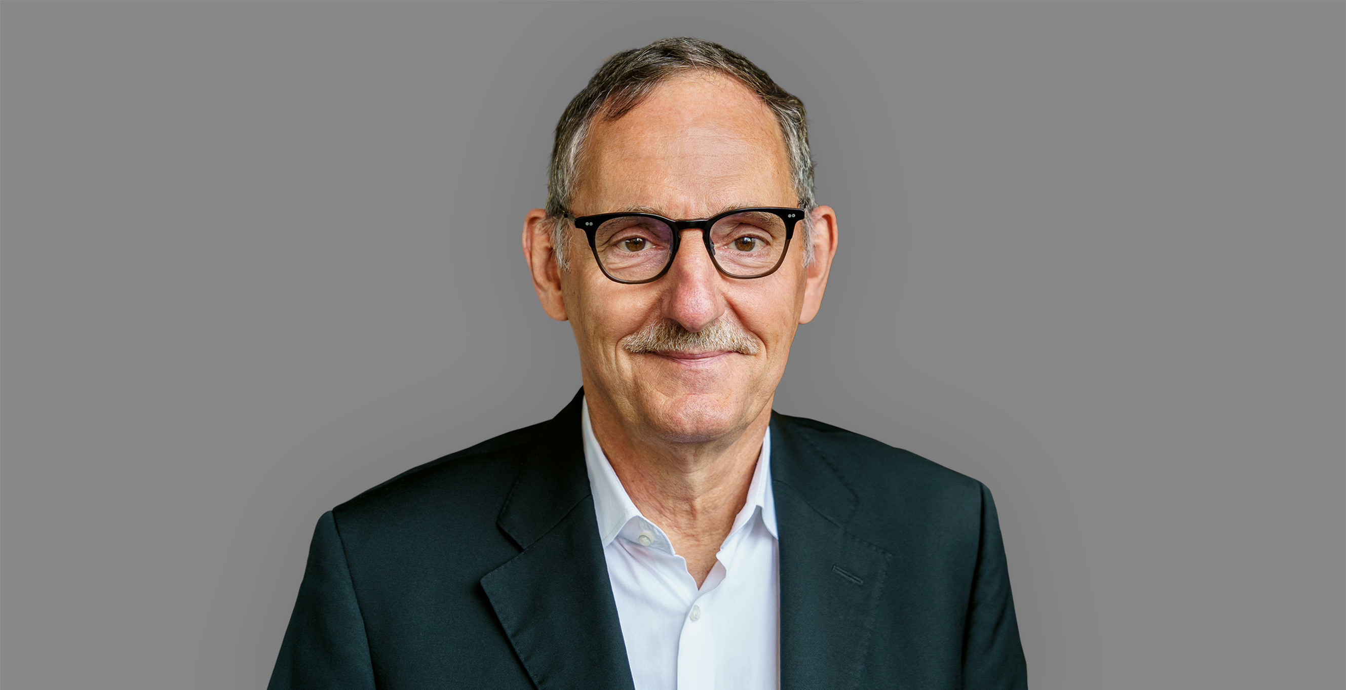Mario Fehr trägt ein schwarzes Jackett und ein weisses Hemd. Er lächelt in die Kamera. 