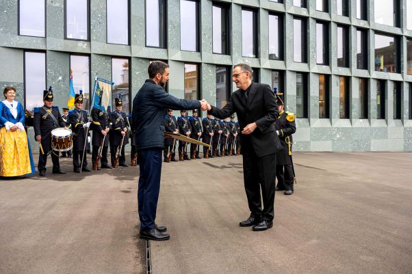 Ins-Amt-Schiessen des neuen Kapo-Kommandanten: Mario Fehr gibt Marius Weyermann die Hand, im Hintergrund das feierliche Prozedere mit zahlreiche Personen mit Gewehr. 