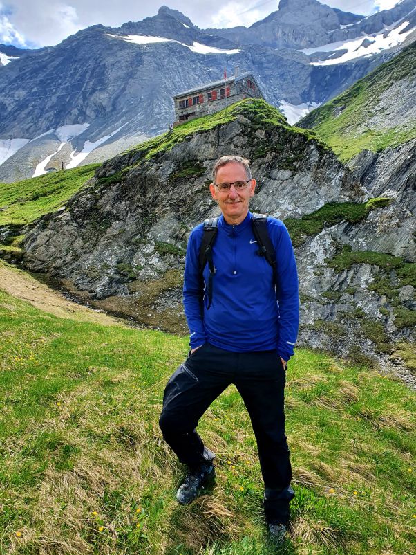 Wandern im Glarnerland: Mario Fehr steht in einer Wiese, hinter ihm Aussicht auf die Berge. 