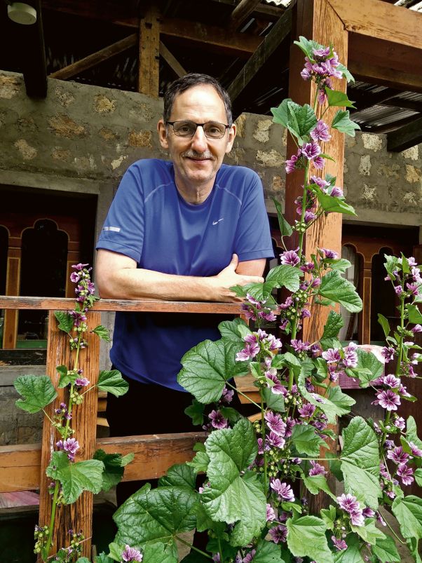 Pause beim Wandern: Mario Fehr stützt sich auf den Holzbalken eines Hauses auf, lacht, vor ihm sind Blumen. 