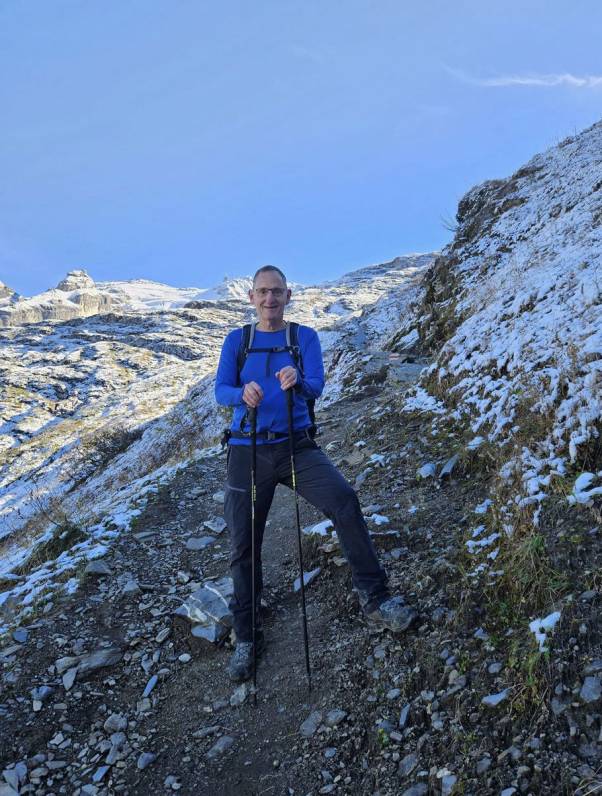 Mario Fehr steht mit Wanderkleidung und Wanderstücken in den Bergen an der Schneegrenze. 