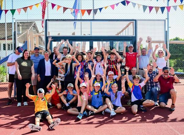 Viele Schülerinnen und Schüler stehen auf dem Sportplatz vor der interaktiven Torwand und jubeln. Darunter befinden sich auch verschiedene Gäste. 
