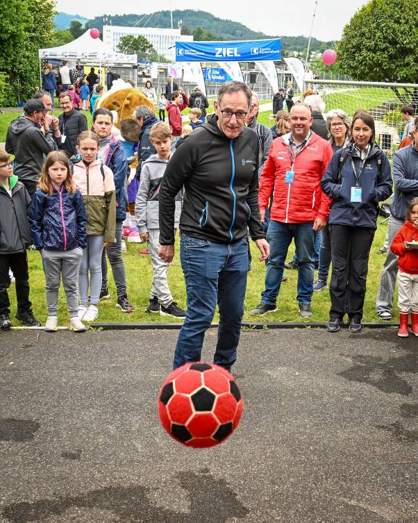 Mario Fehr schiesst einen roten Fussball in Richtung Kamera. Er schaut sehr konzentriert. Im Hintergrund schauen viele Personen zu.