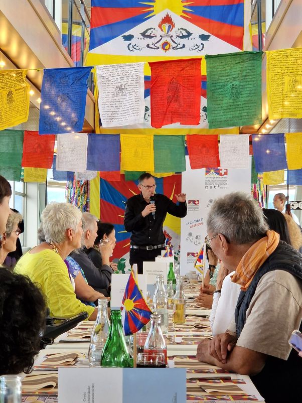 Anlass Gesellschaft Schweizerisch-Tibetische Freundschaft: Mario Fehr richtet Worte an die Gäste, an dem Tisch vor ihm sitzen zahlreiche Personen und hören zu. 
