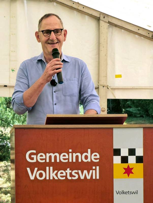 Mario Fehr steht am Rednerpult, hält das Mikrofon in der Hand und lacht. Auf dem Rednerpult steht «Gemeinde Volketswil».
