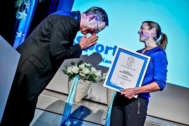 Verleihung Sportpreis des Kantons Zürich 2022: Mario Fehr verneigt sich auf der Bühne vor Siegerin Nicola Spirig, die die Sportpreis-Urkunde in den Händen hält. 