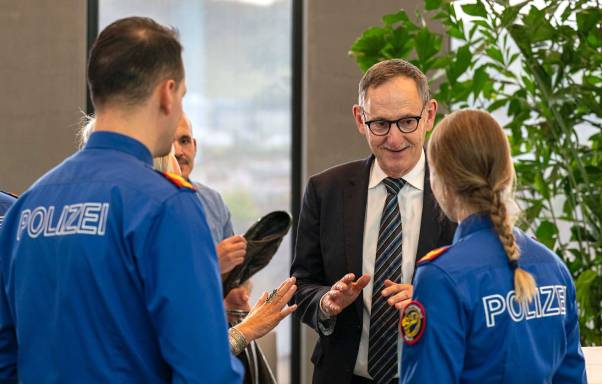 Mario Fehr steht neben einem Polizist und einer Polizistin und spricht lächelnd mit ihnen. Fehr trägt einen schwarzen Anzug mit einer gestreiften Krawatte. Die Polizistin und der Polizist stehen mit dem Rücken zur Kamera und tragen eine blaue Uniform.