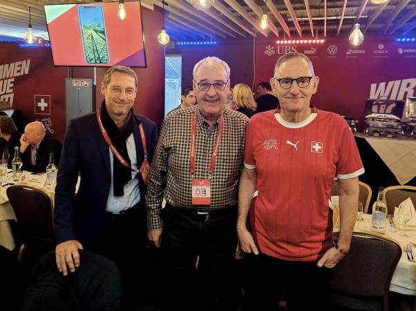 Urs Wiedmer, Guy Parmelin und Mario Fehr stehen nebeneinander und lachen in die Kamera. Wiedmer trägt ein schwarzes Jackett, Parmelin ein kariertes Hemd und Fehr ein rotes Nati-Trikot. 