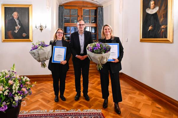 Doris Keller und Marion Daube halten Blumensträusse und die Sportpreis-Urkunde in ihren Händen. Sie lachen fröhlich in die Kamera. In der Mitte steht Mario Fehr. Hinter ihnen hängen Gemälde in einem Raum des Rathauses Zürich. 