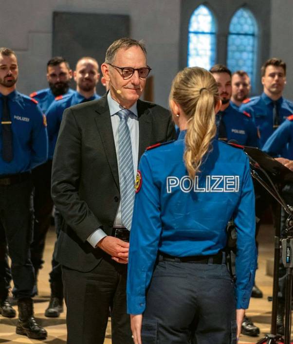 Eine Polizei-Aspirantin steht in Uniform mit dem Rücken zur Kamera. Hinter ihr ist lächelnd Mario Fehr zu sehen. Daneben stehen weitere Aspiranten. 
