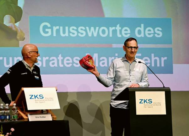 Mario Fehr steht am Rednerpult. Er lacht und hält ein Herz mit Teigwaren darin in der Hand. 